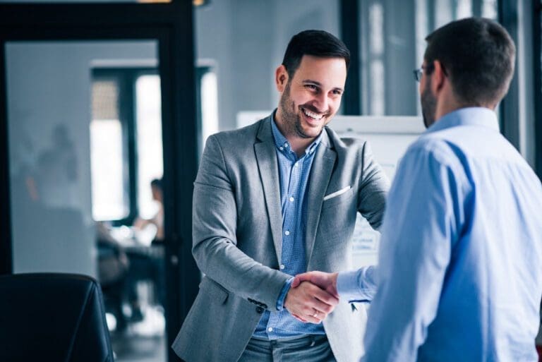 two smiling businessmen shaking hands while standing office